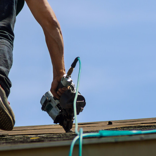 A roofer installs shingles with nail gun.